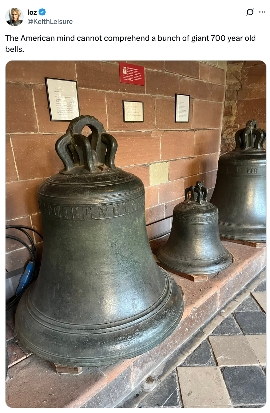 Three large ancient bells displayed on a stone floor with informational signage on the wall above