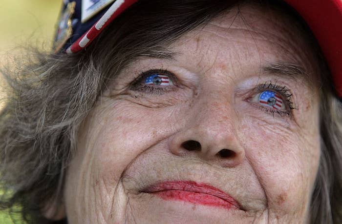 Elderly pistillate smiling, wearing a reddish headdress with flag-patterned glasses that bespeak an American emblem plan connected her eyes