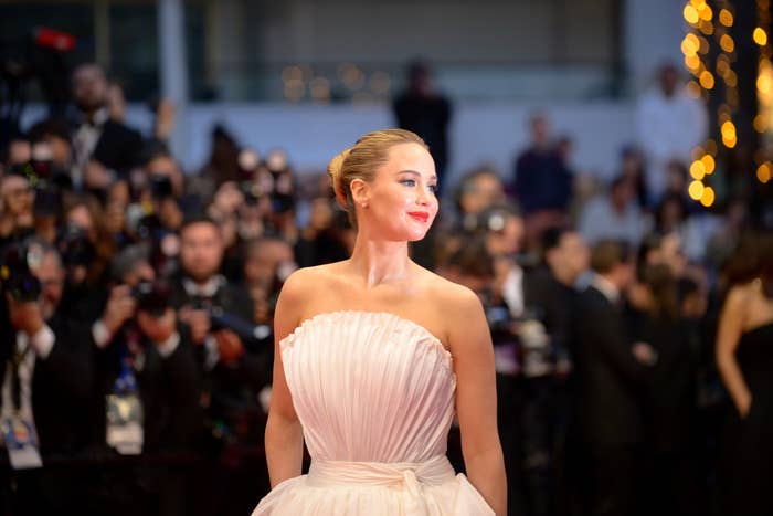 Jennifer Lawrence on a red carpet wearing a strapless gown, surrounded by photographers taking pictures