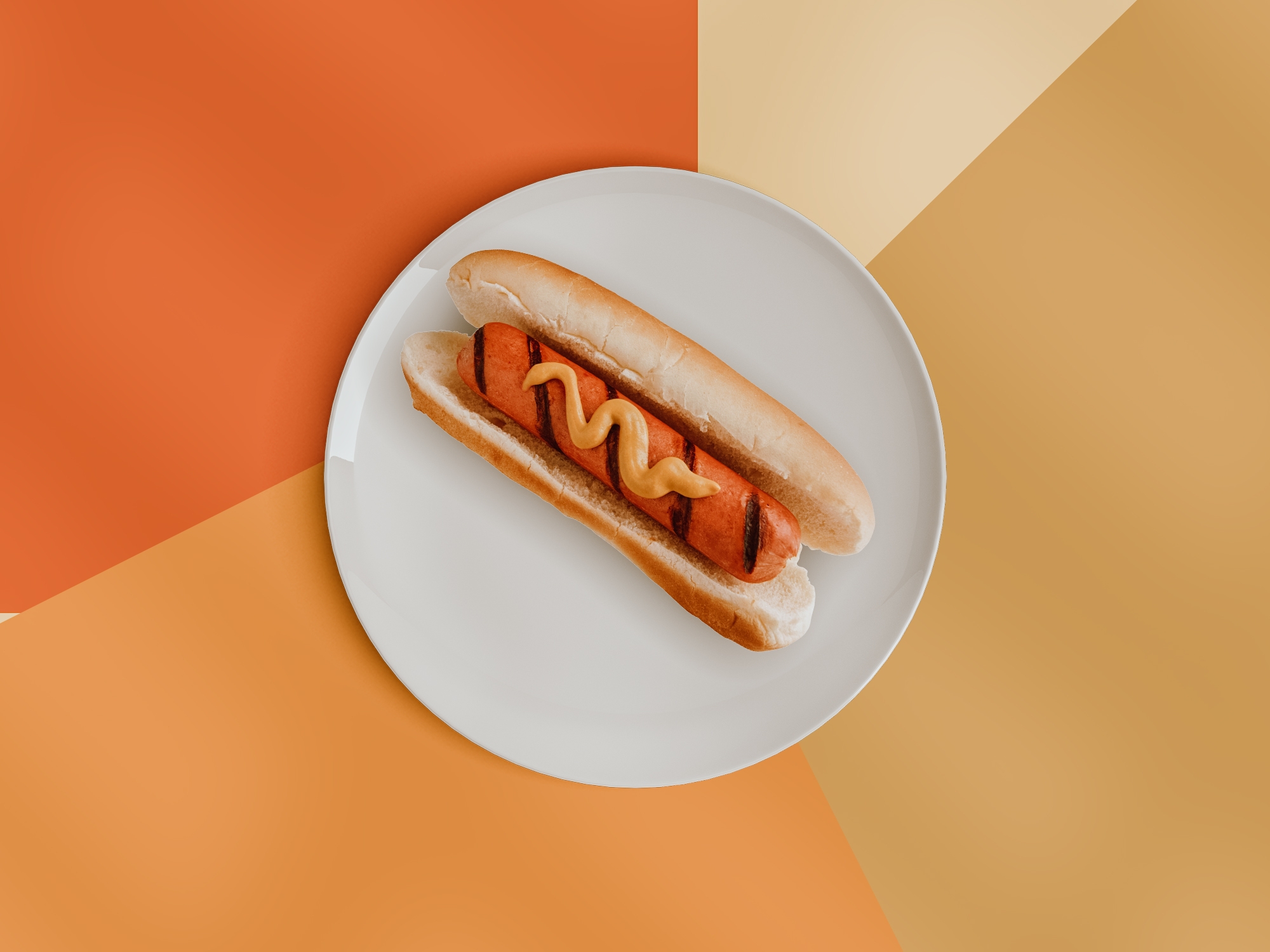 Hothund med sennep på en hvit tallerken, satt mot en geometrisk oransje og beige bakgrunn