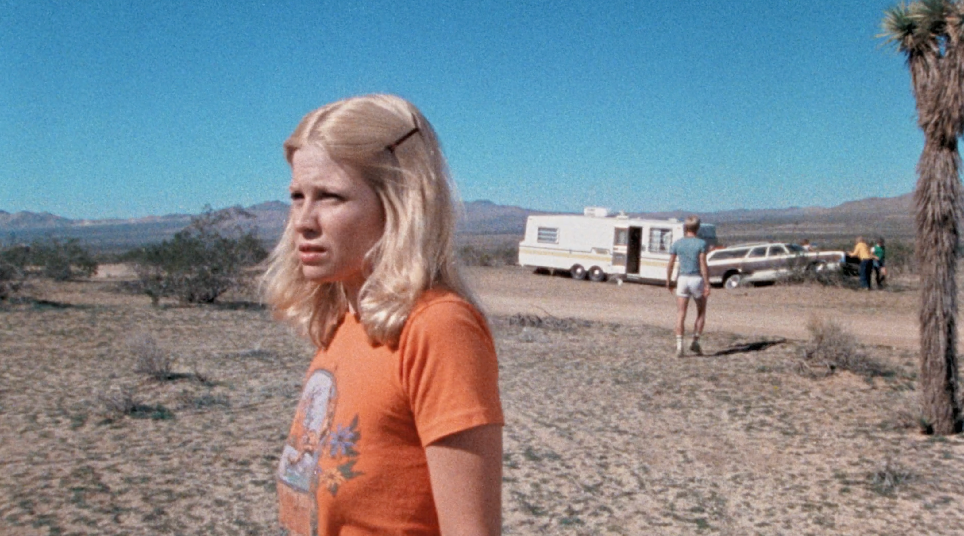 In a still from &quot;The Hills Have Eyes,&quot; a blonde woman stares into the distance in a desert setting with a trailer in the background
