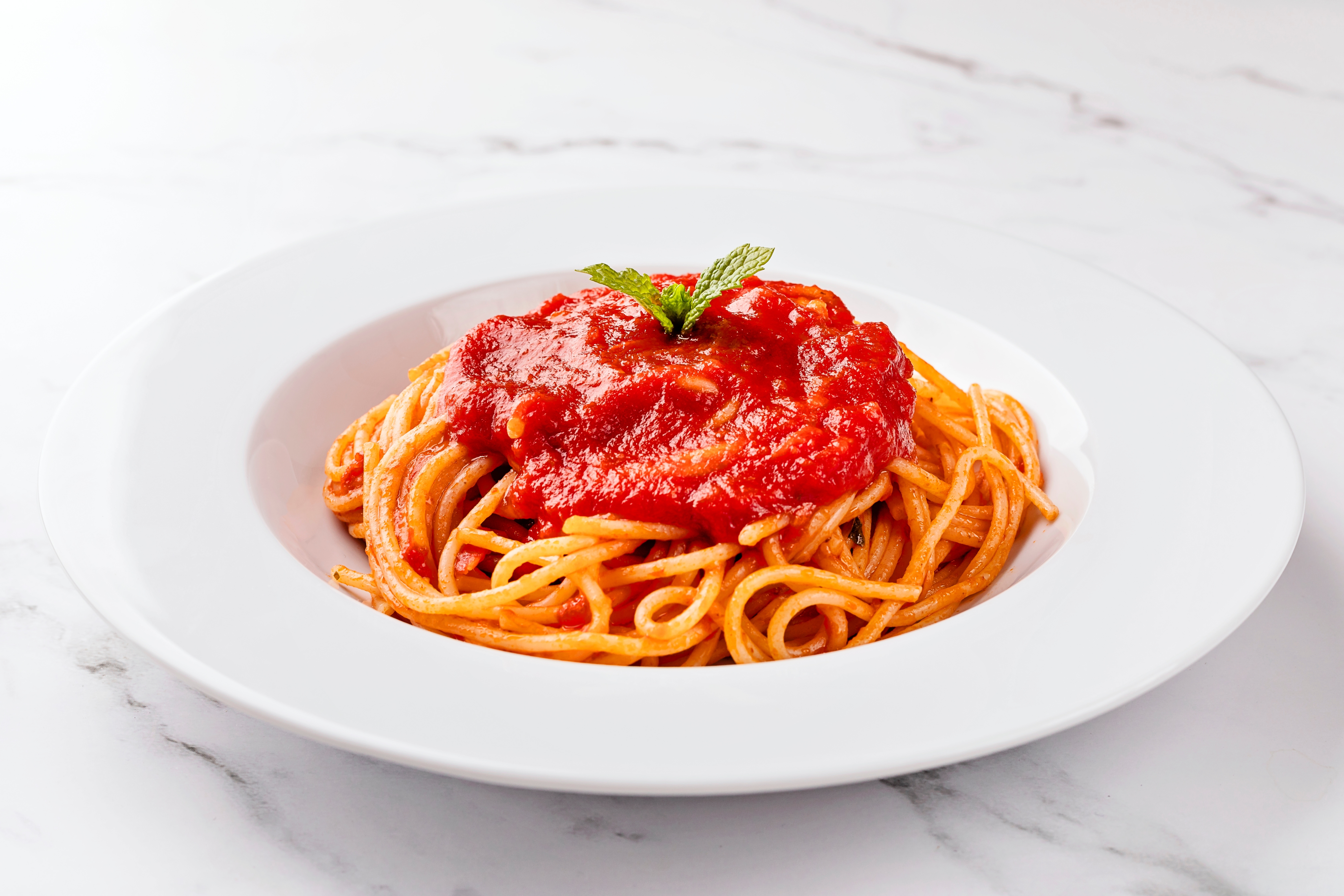 En tallerken med spaghetti toppet med marinarasaus og pyntet med et mynteblad på en marmoroverflate