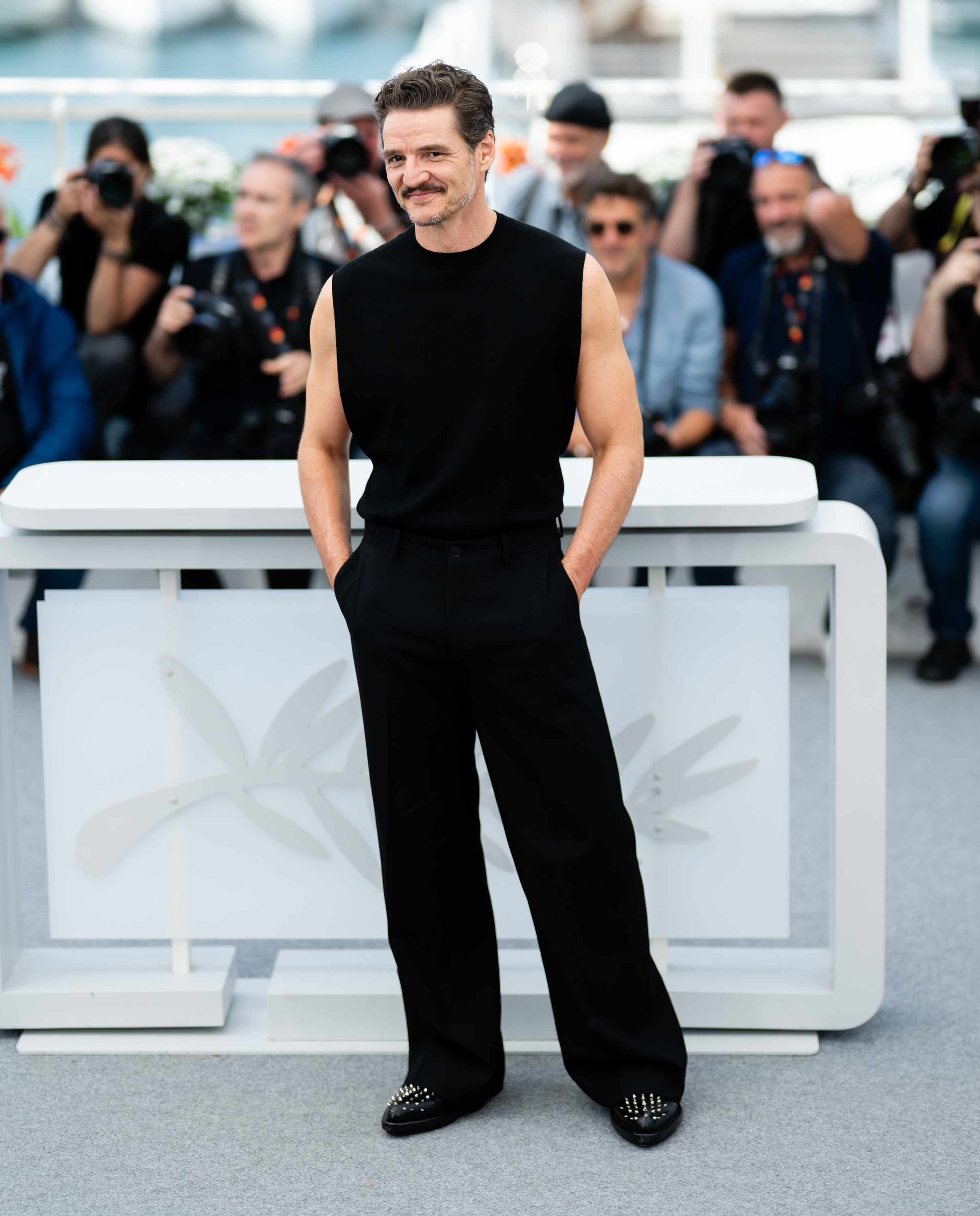 A person in a sleeveless black top and wide-leg pants poses confidently in front of photographers