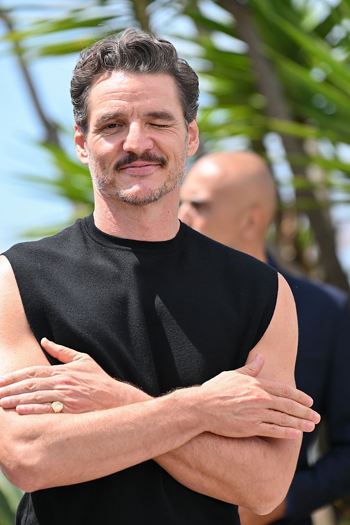 A person smiling with arms crossed, wearing a sleeveless top, winking at the camera outdoors