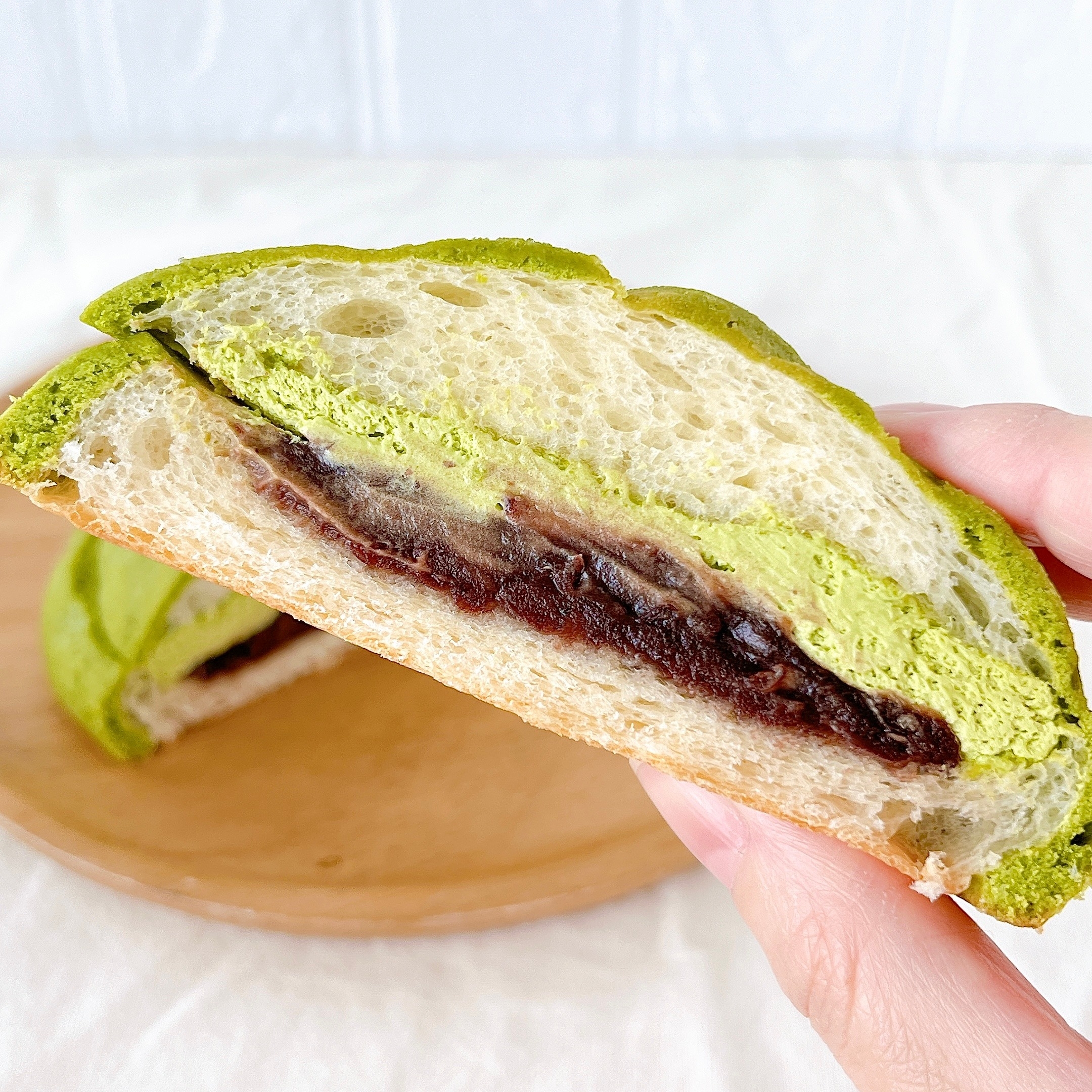 パンの断面。抹茶味のパン生地に、あんこが詰まっている様子。手で持っている。