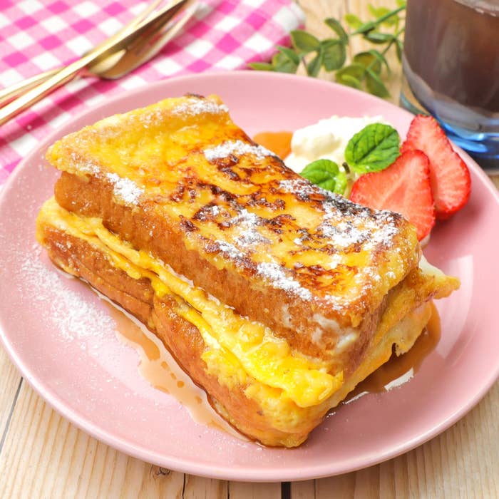 フレンチトーストの上にパウダーシュガー、横にクリームとイチゴが添えられている朝食の一皿。