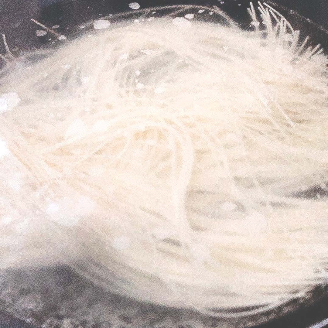 鍋で茹でている麺。泡立つ湯が見える。食材の調理過程を示す。