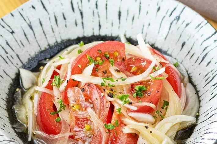 トマトと玉ねぎのサラダが大皿に盛り付けられている。細かく刻んだハーブが振りかけられている。