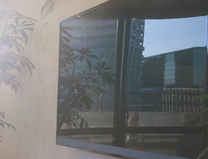 Modern living room with a large leather sectional, flat-screen TV, and bright sunlight streaming through floor-to-ceiling windows