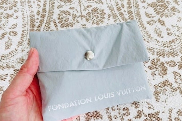 手に持たれたLouis Vuittonの封筒。背景に模様のある布が敷かれている。