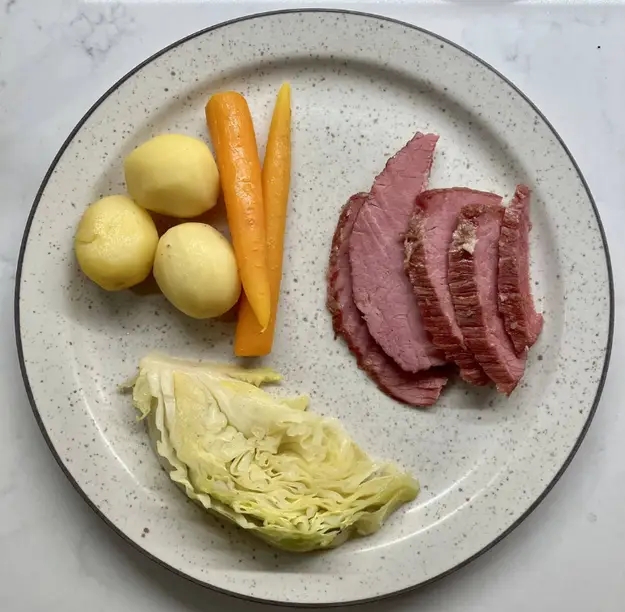 Plate with sliced corned beef, whole boiled potatoes, carrot sticks, and a wedge of cabbage