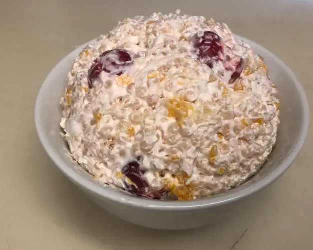Fruit salad with whipped cream in a bowl, featuring visible grapes and oranges