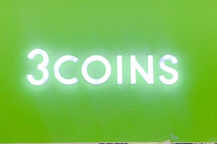 店の入り口上部に「3COINS」と書かれた看板。下には商品の割引案内がある。