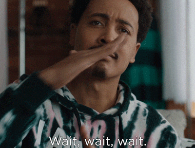 Person in patterned hoodie making a "wait" gesture with their hand. Subtitles read: "Wait, wait, wait."