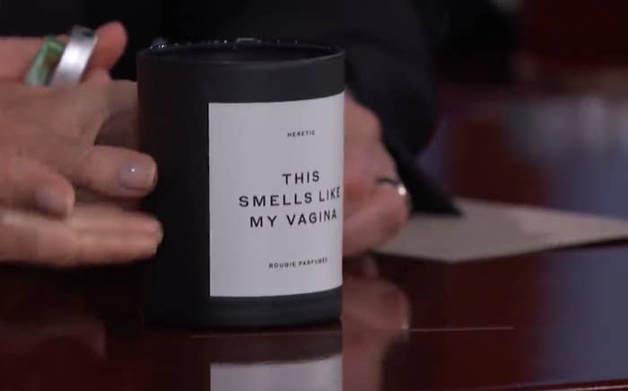 A candle labeled "This Smells Like My Vagina" on a table during an interview