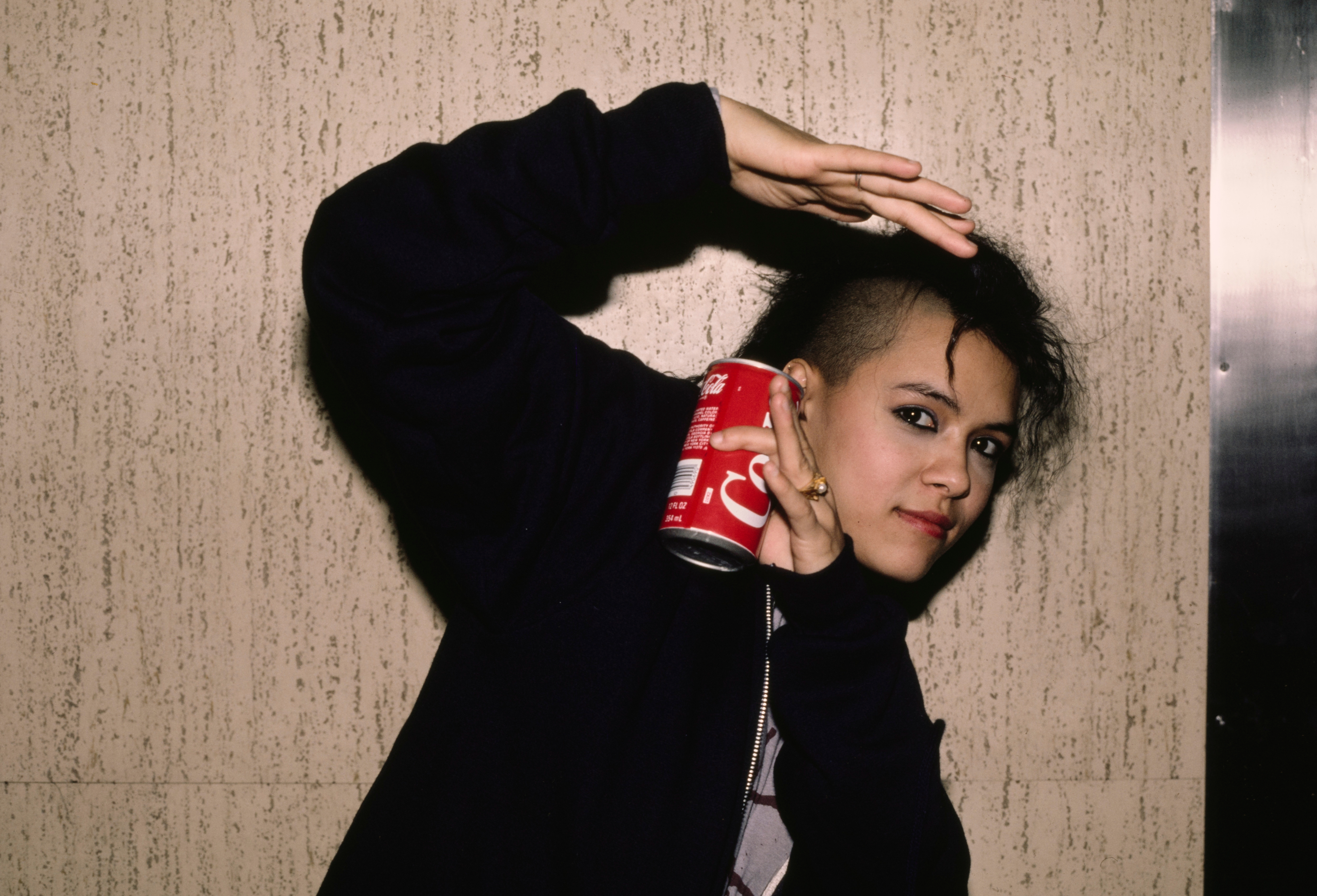 Person playfully holding a soda can by their head, posing with one arm curved above