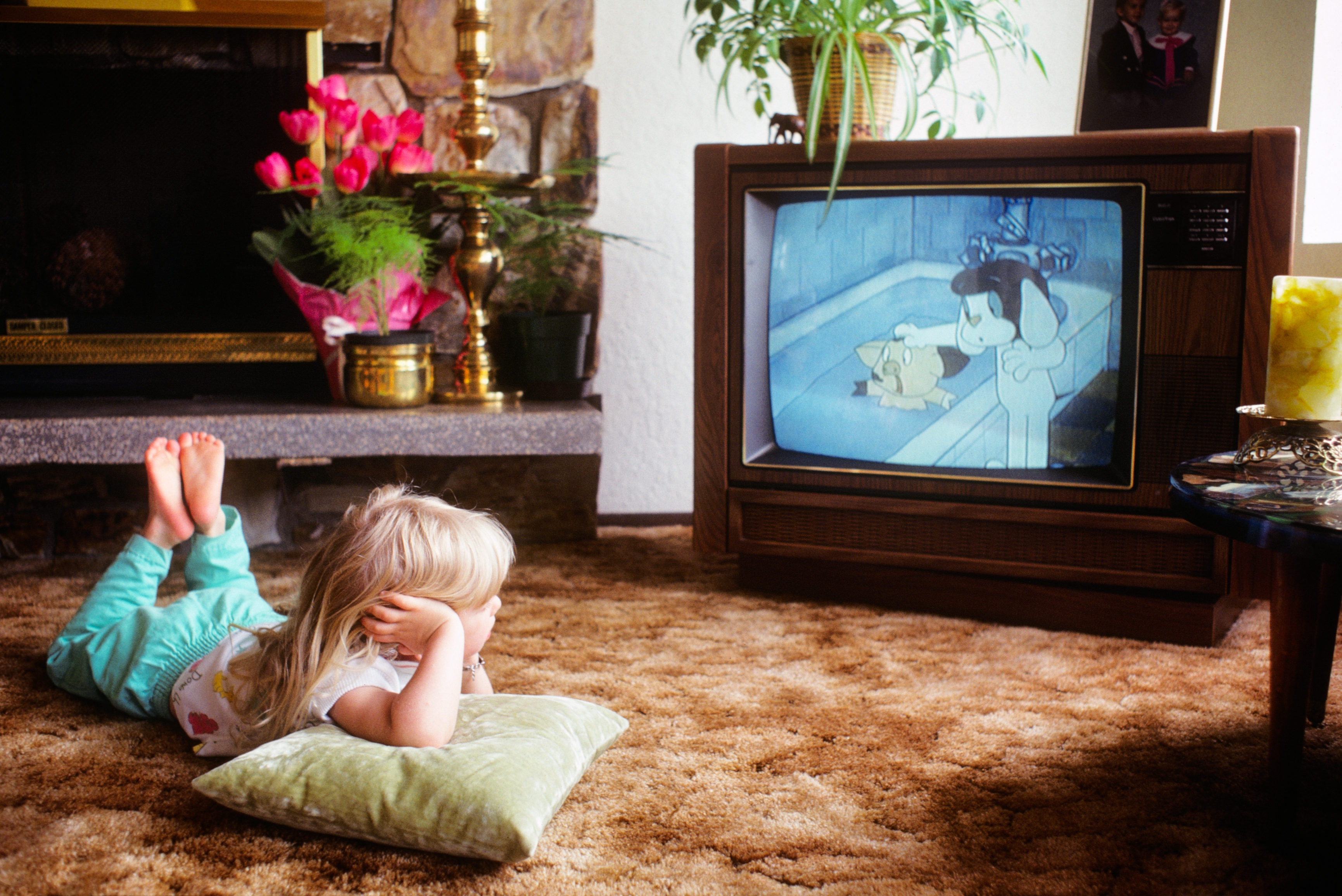 Child lying on carpet, watching an animated cartoon on an old-fashioned TV set in a cozy living room