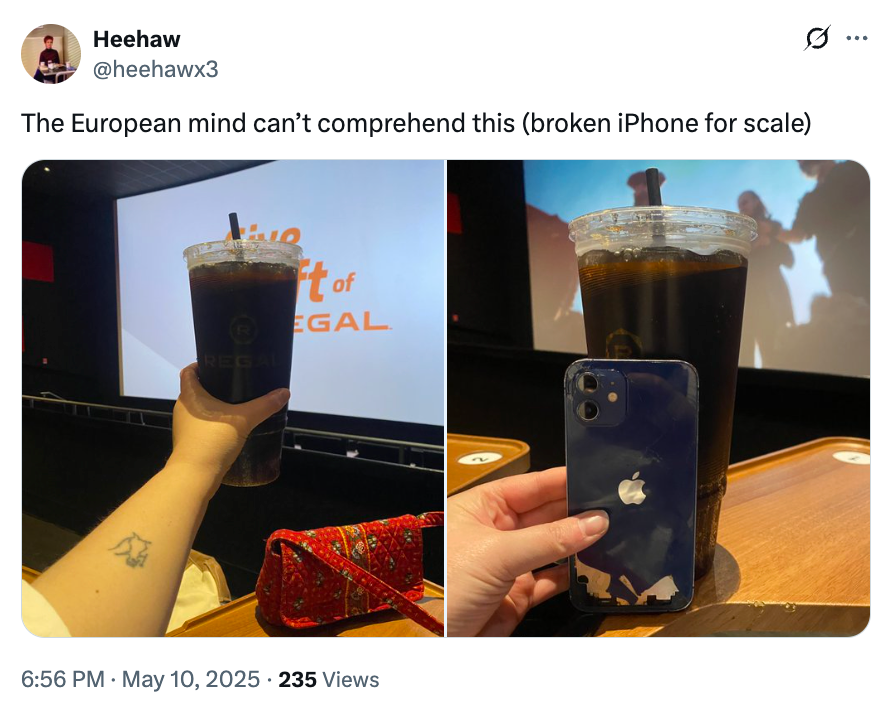 A large drink cup and a broken iPhone are held in a theater, with a screen displaying text in the background