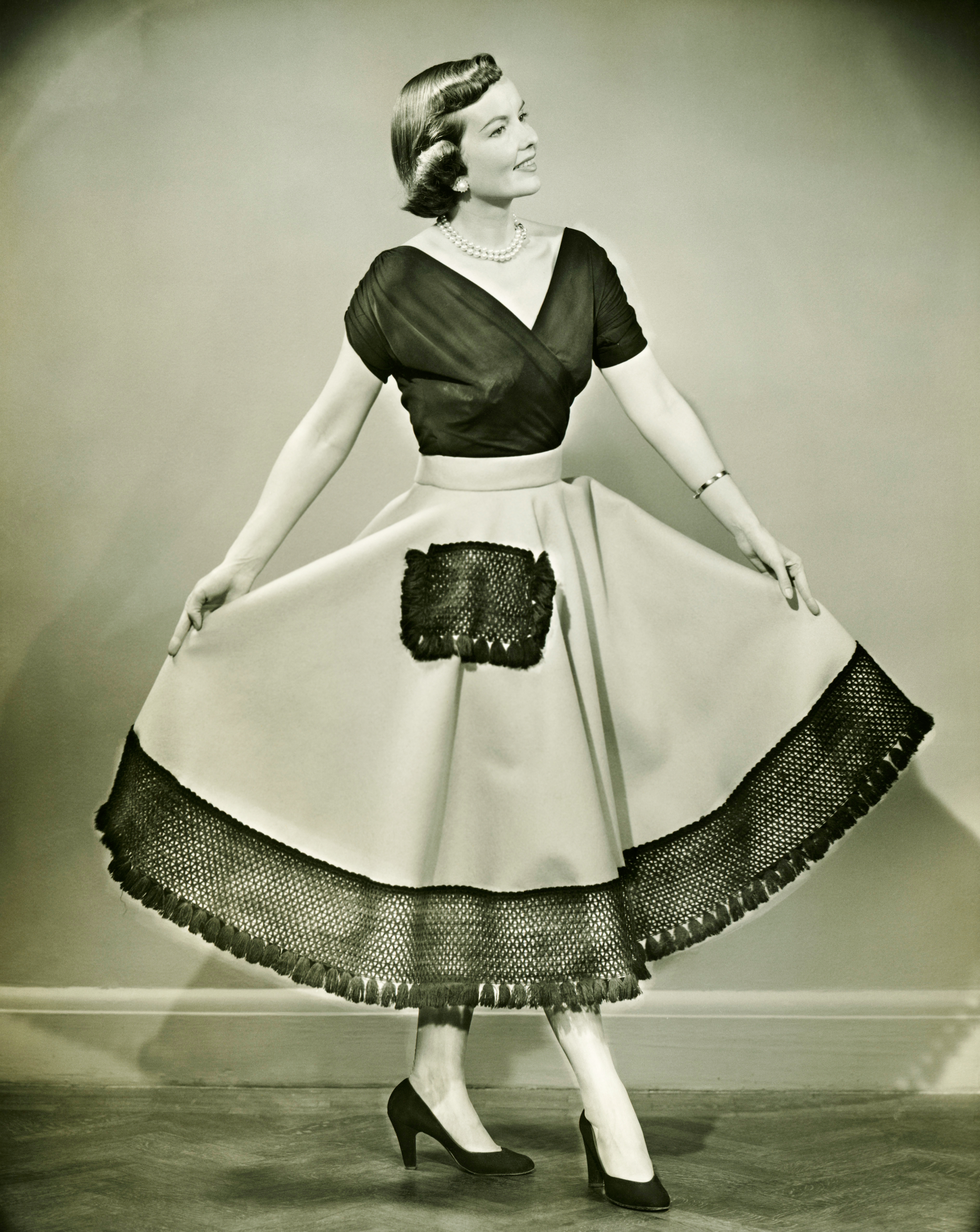 Woman in vintage dress with a cinched waist, fitted top, and full skirt with lace trim, posing gracefully indoors