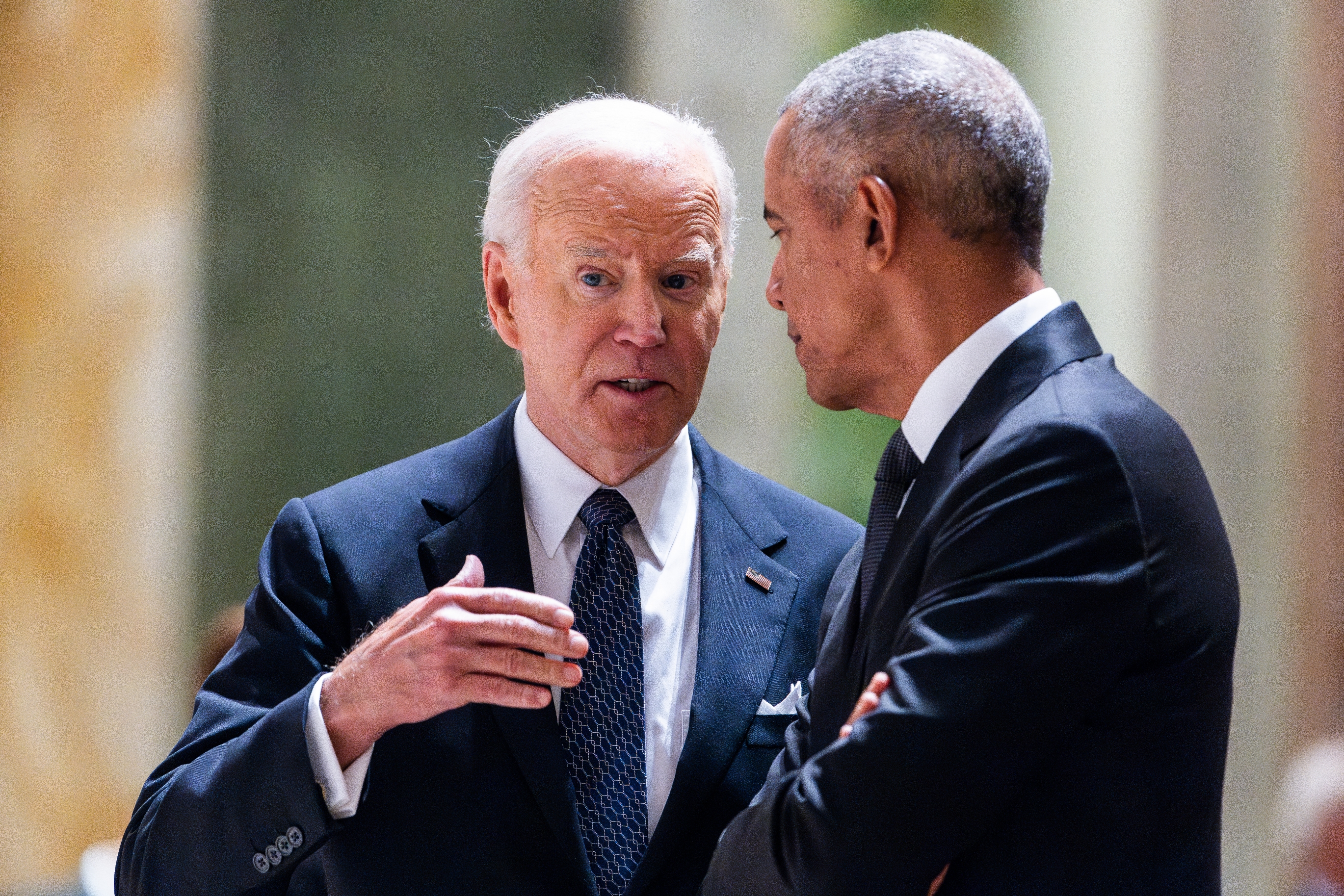 Two men in suits have a serious discussion at an elegant event. One gestures while speaking to the other who listens attentively