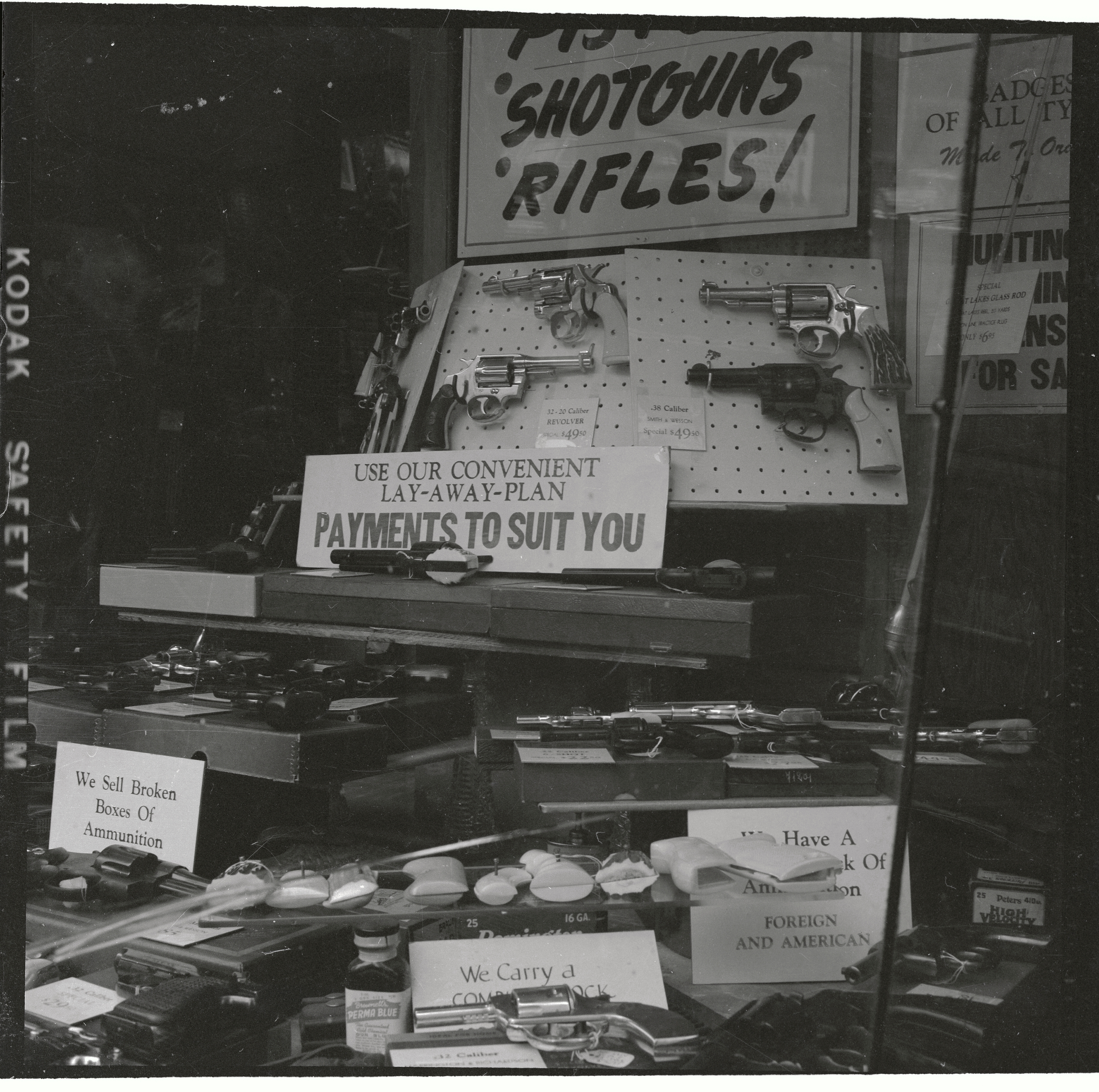 Store window display featuring various firearms and ammunition with signs about payment plans and ammunition availability