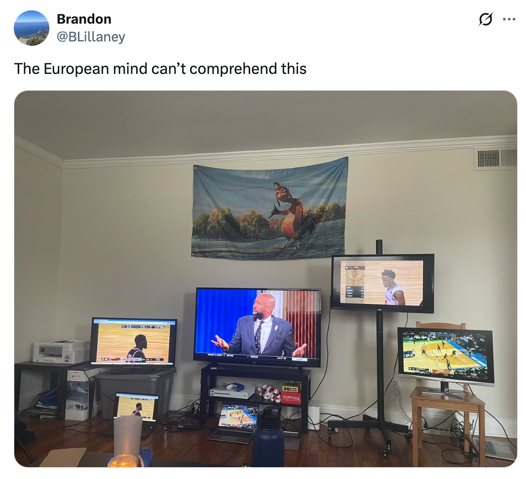 Room with multiple screens showing sports and a game show, with a tapestry above