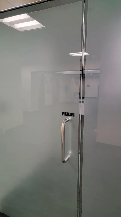 Glass door with "PULL" sign and a metal handle, revealing an office interior with overhead lights in the background
