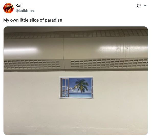 A small window poster on a plain wall depicts a tropical beach with a palm tree, creating an illusion of paradise