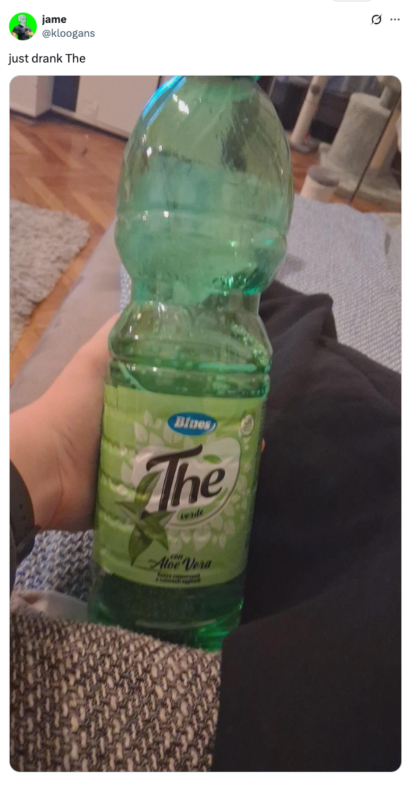 A hand holding a bottle of "The" brand aloe vera green tea drink indoors