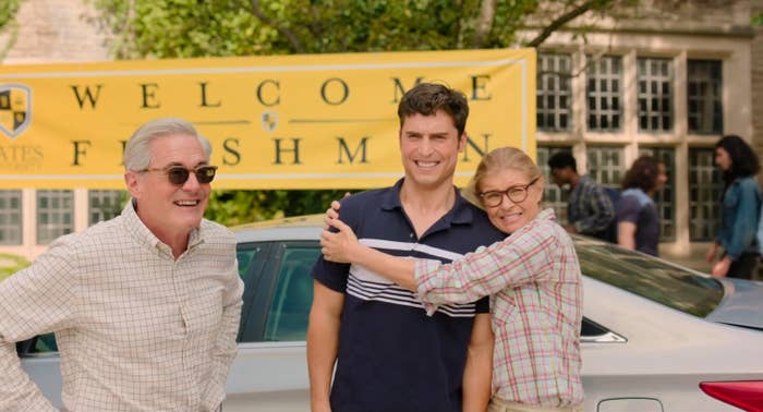 Three people stand smiling in front of a "Welcome Freshman" banner outside a building. One person hugs another warmly