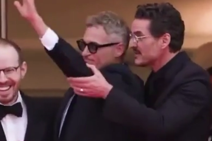 Three men in formal suits on a red carpet, one waving
