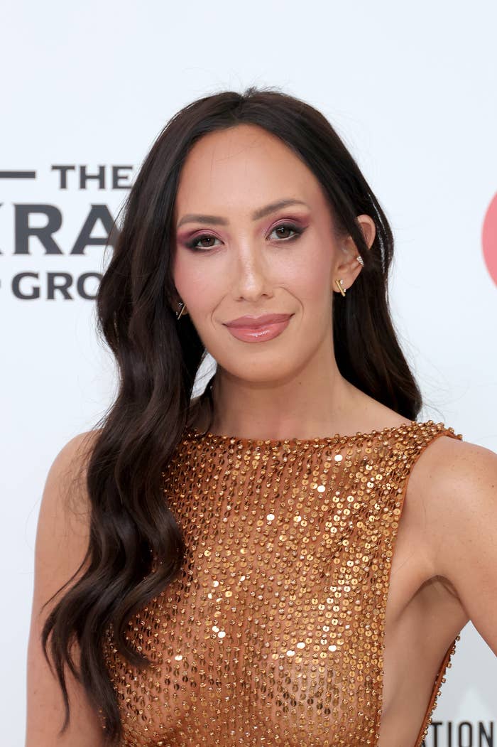 Cheryl Burke in elegant, beaded gown with long, wavy hair, standing against a backdrop with text