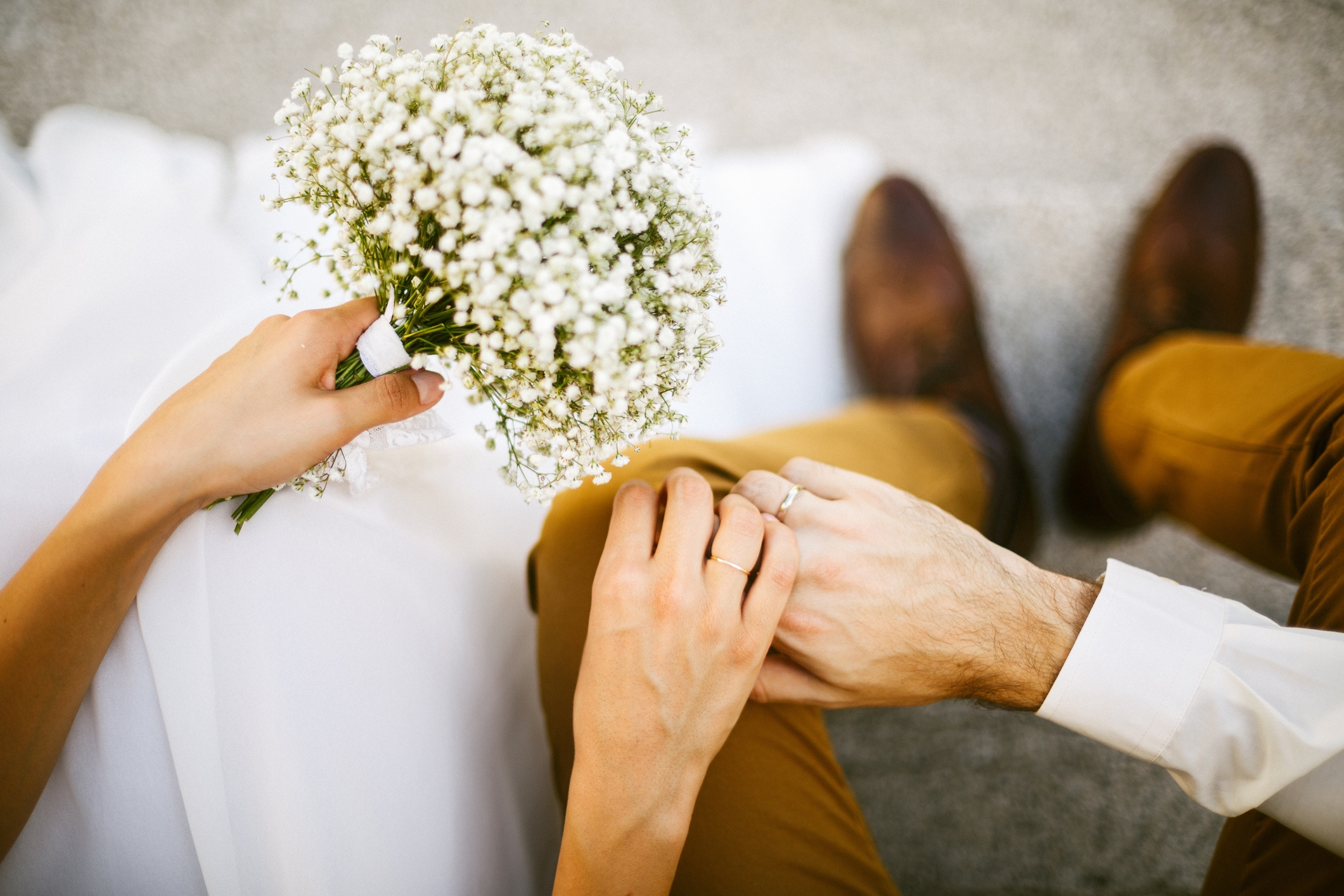 Et par sitter tett og holder hender. Den ene holder en bukett med små hvite blomster, noe som antyder en romantiker eller bryllupsscene