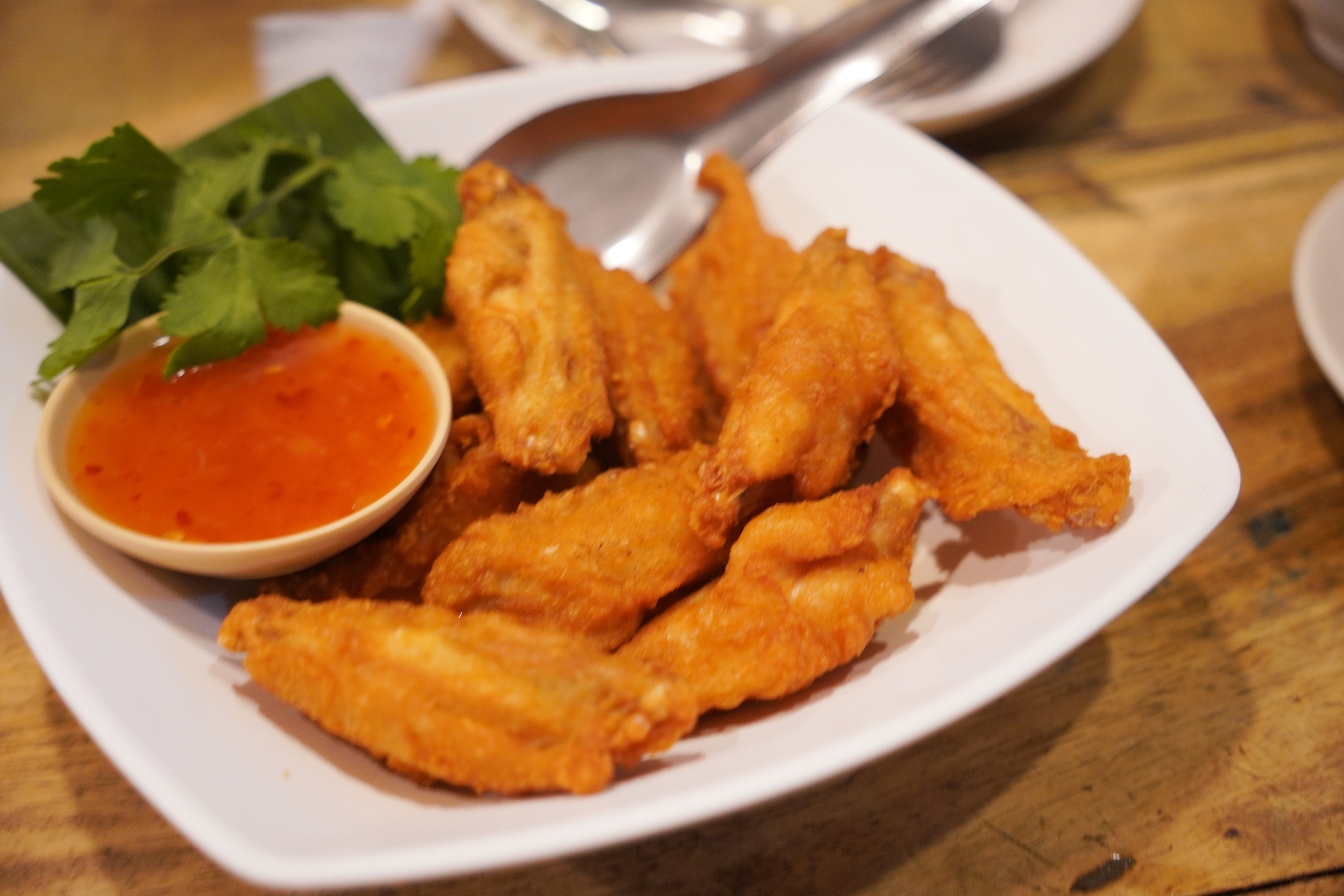 Plate of crispy fried chicken wings with a side of dipping sauce and garnished with fresh herbs