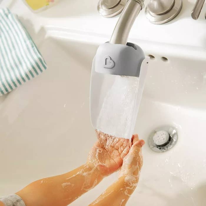 A kid rinses their hands nether an extended faucet spout successful a sink, demonstrating a merchandise that helps young children scope moving h2o easily