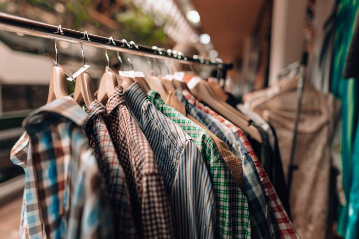 Shirts on wooden hangers in a clothing store, arranged neatly on a rack, showcasing various patterns like plaid and stripes