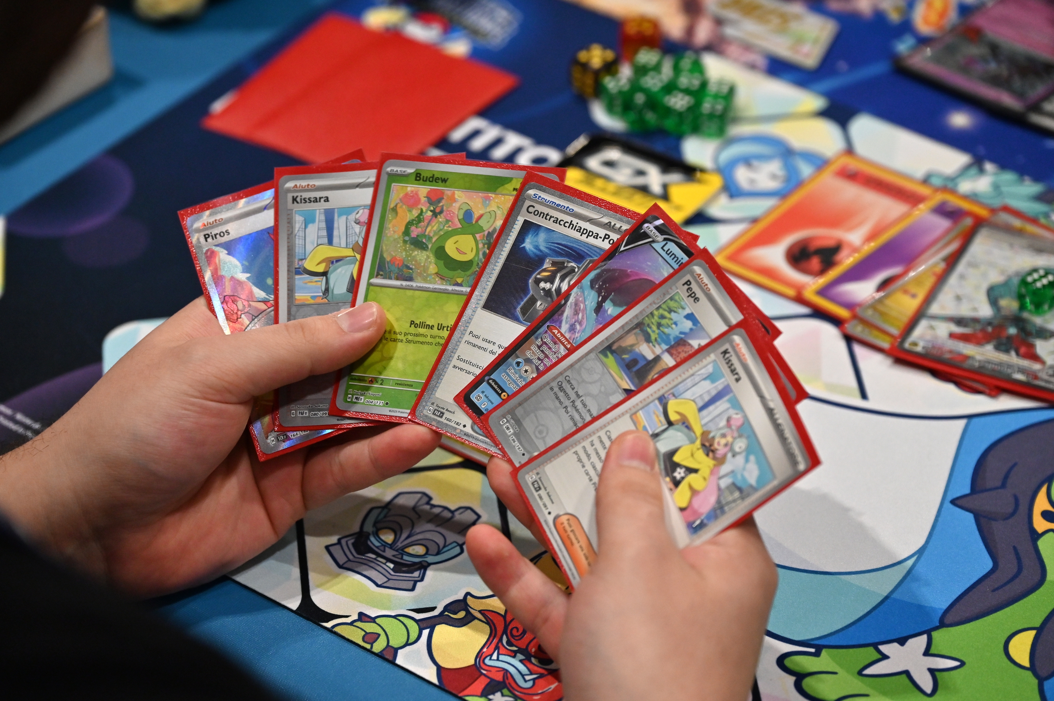 Person holding playing cards from a collectible card game, with colorful cards and gaming accessories on the table