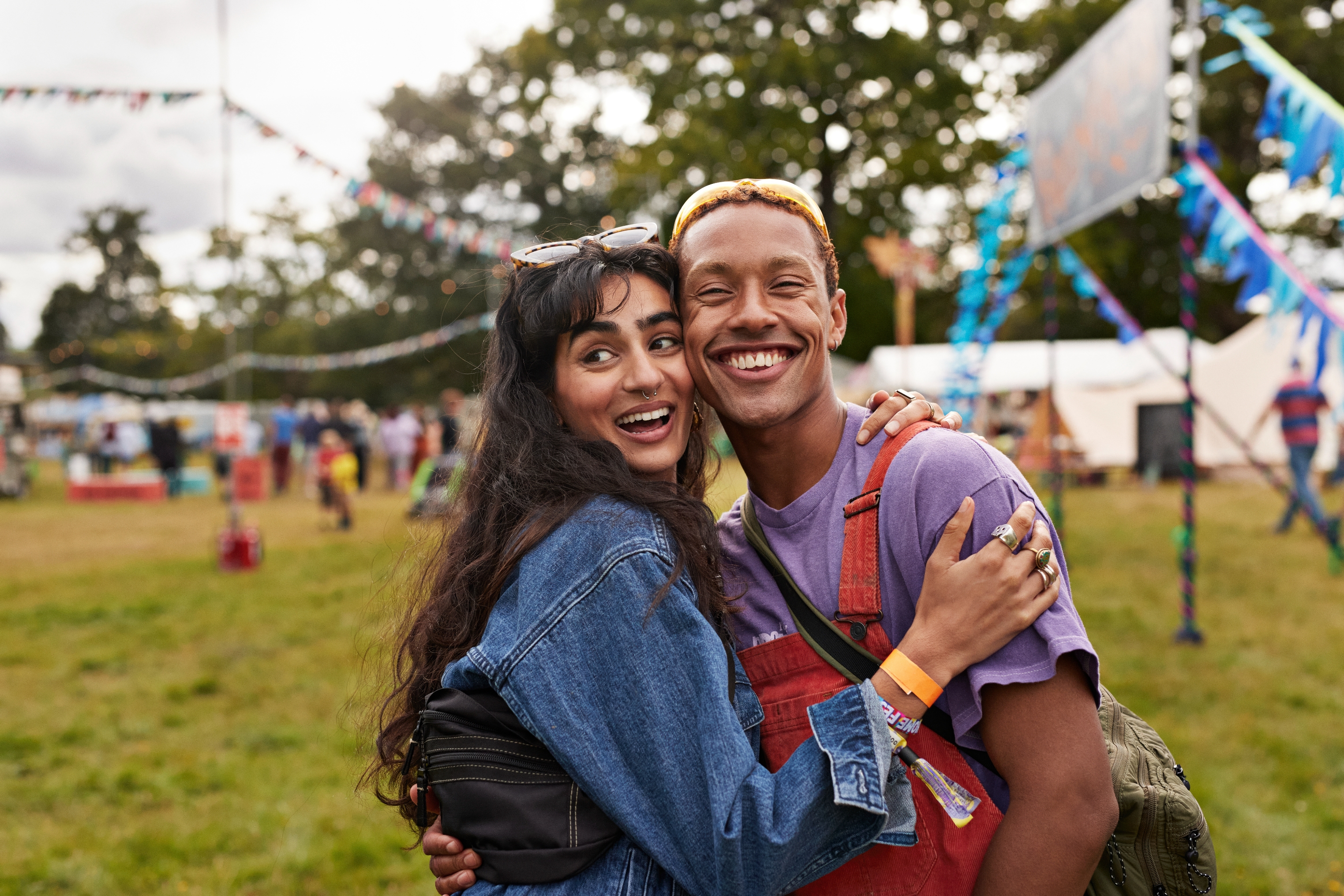 Two people happily embrace outdoors at a festival, both dressed casually