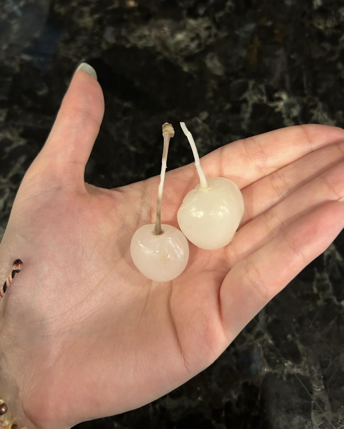 Two peeled cherries held in an open hand against a dark background