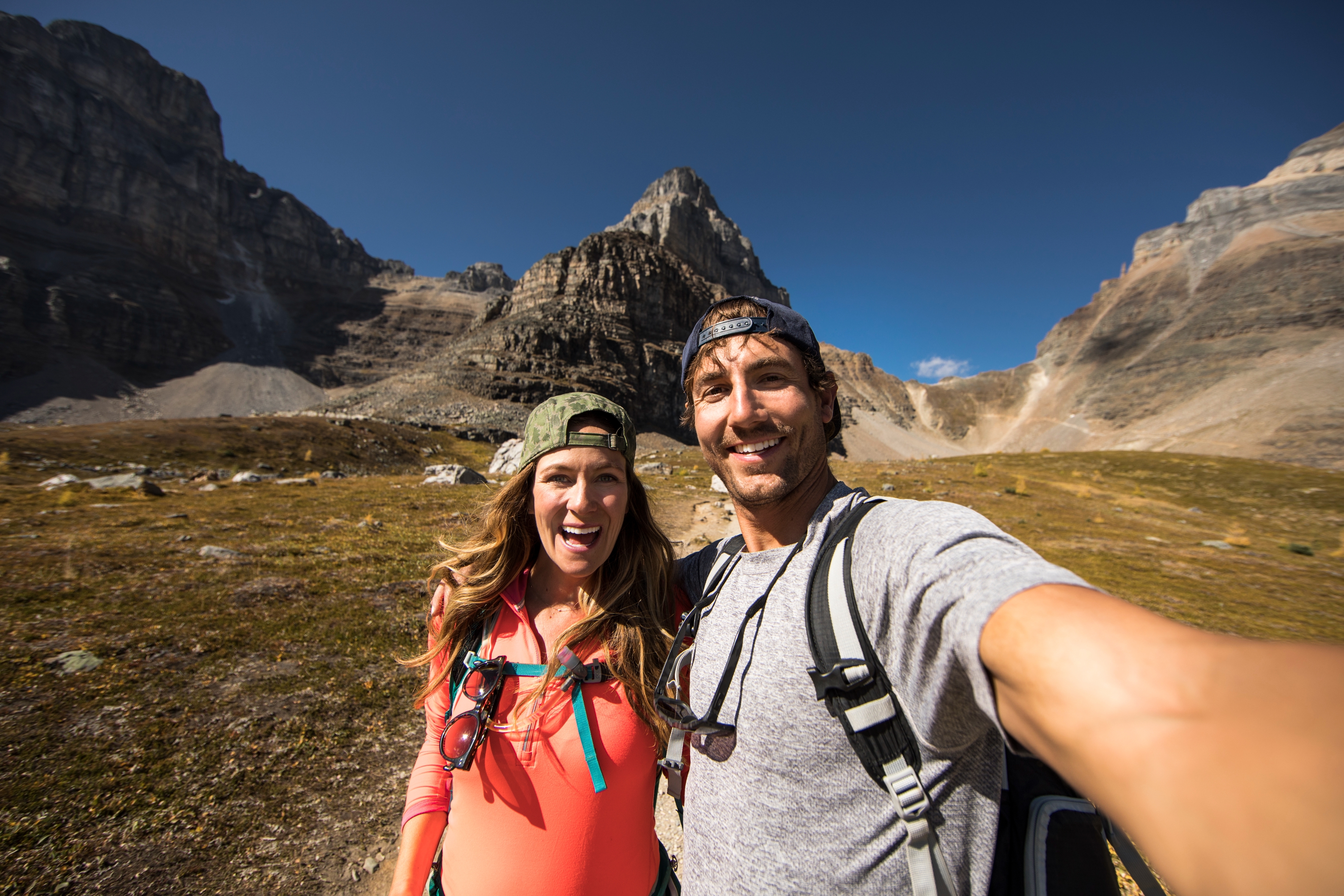 A couple takes a happy selfie during a mountain hike, surrounded by rugged terrain and clear skies