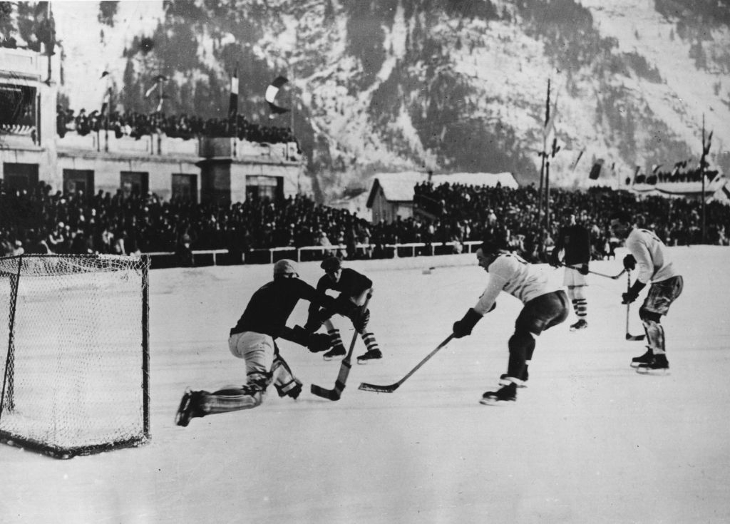 Historic hockey game on an outdoor ice rink with snow-covered mountains in the background; players and goal in action