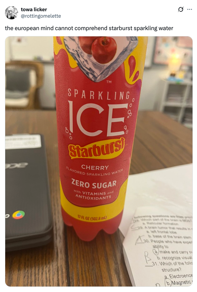 A bottle of Starburst-flavored sparkling water on a table beside an open laptop and papers
