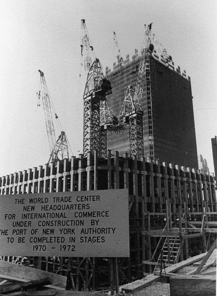 Construction of World Trade Center in progress, with cranes atop a partially completed building. Sign details construction timeline: 1970-1972
