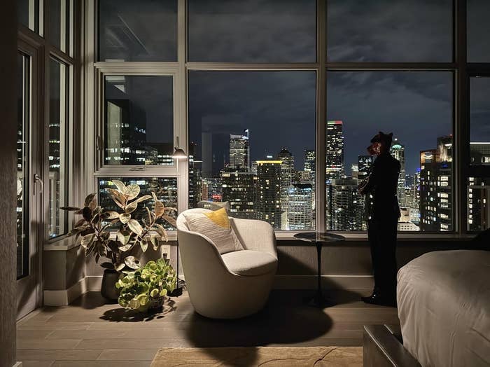 A idiosyncratic gazes retired the model of a modern high-rise flat astatine a metropolis skyline lit up astatine night, lasting adjacent a plush seat and houseplants