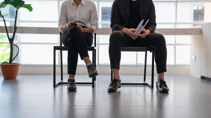Two people in business attire sit in a waiting area, suggesting a job interview or business meeting setting