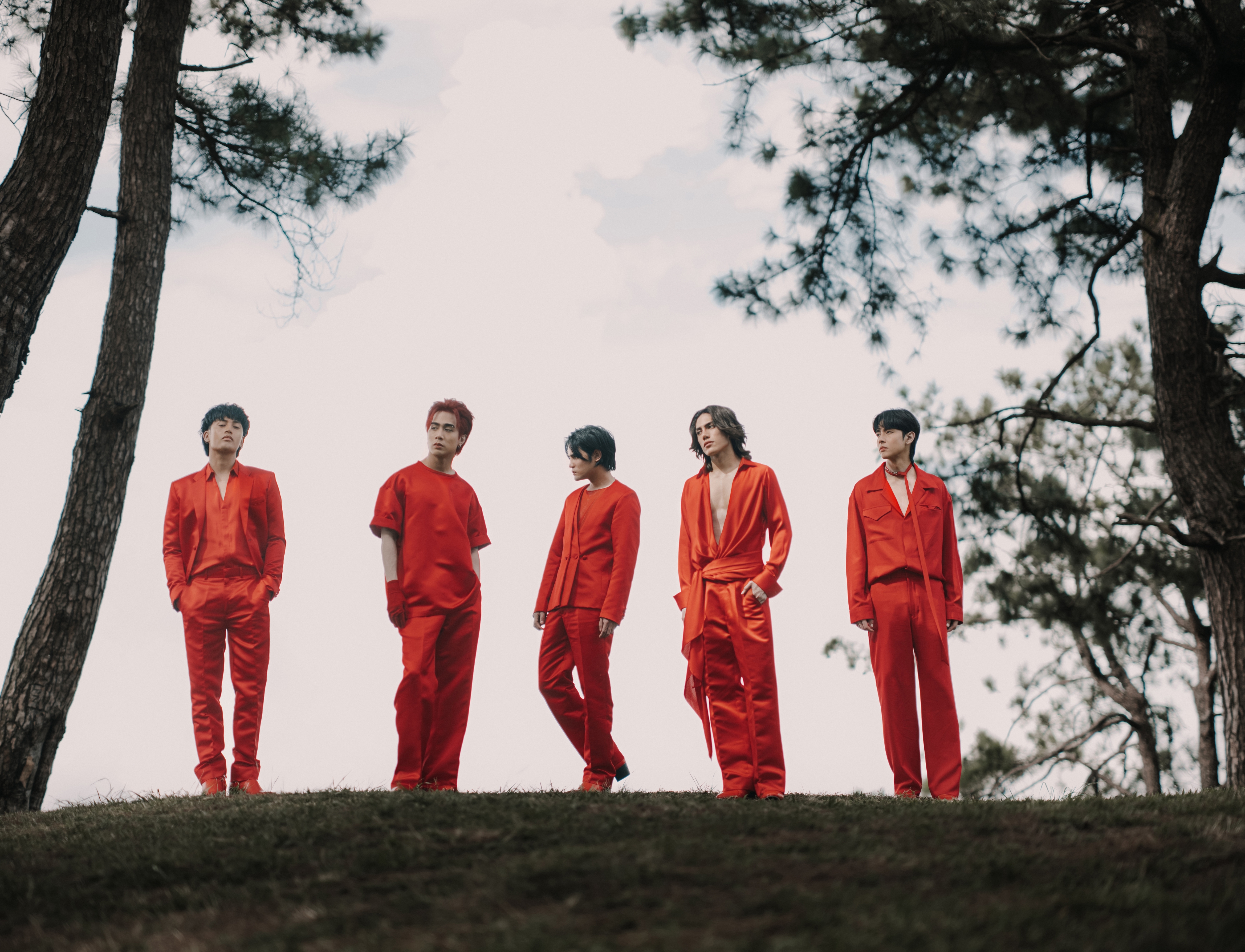 Five people in red outfits stand outdoors, framed by trees, posing stylishly