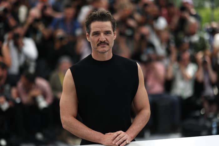 Persona con bigote, usando camiseta sin mangas, posa frente a fotógrafos en un evento público