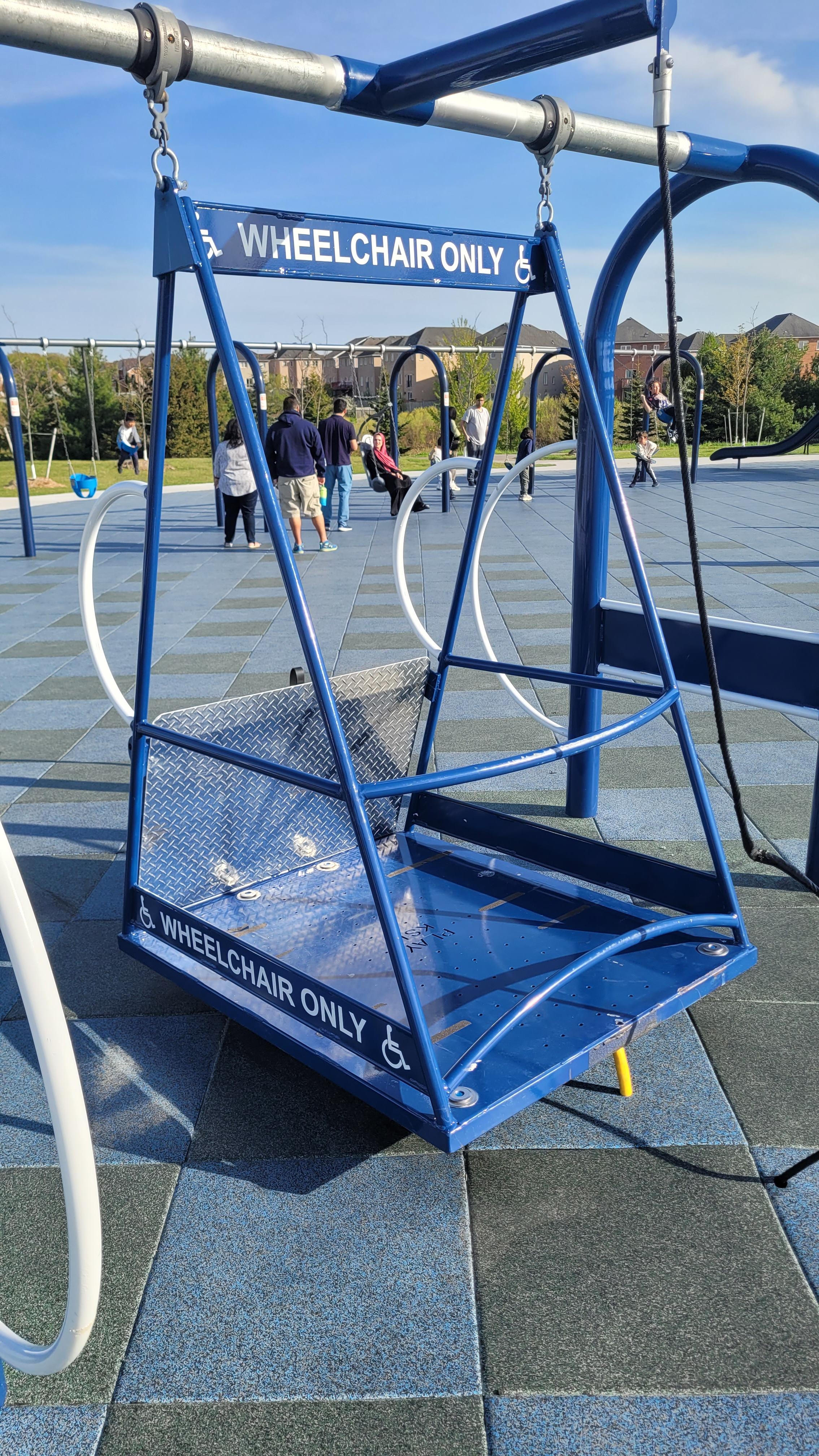 Playground swing labeled "Wheelchair Only," designed for accessibility, located in an outdoor park setting