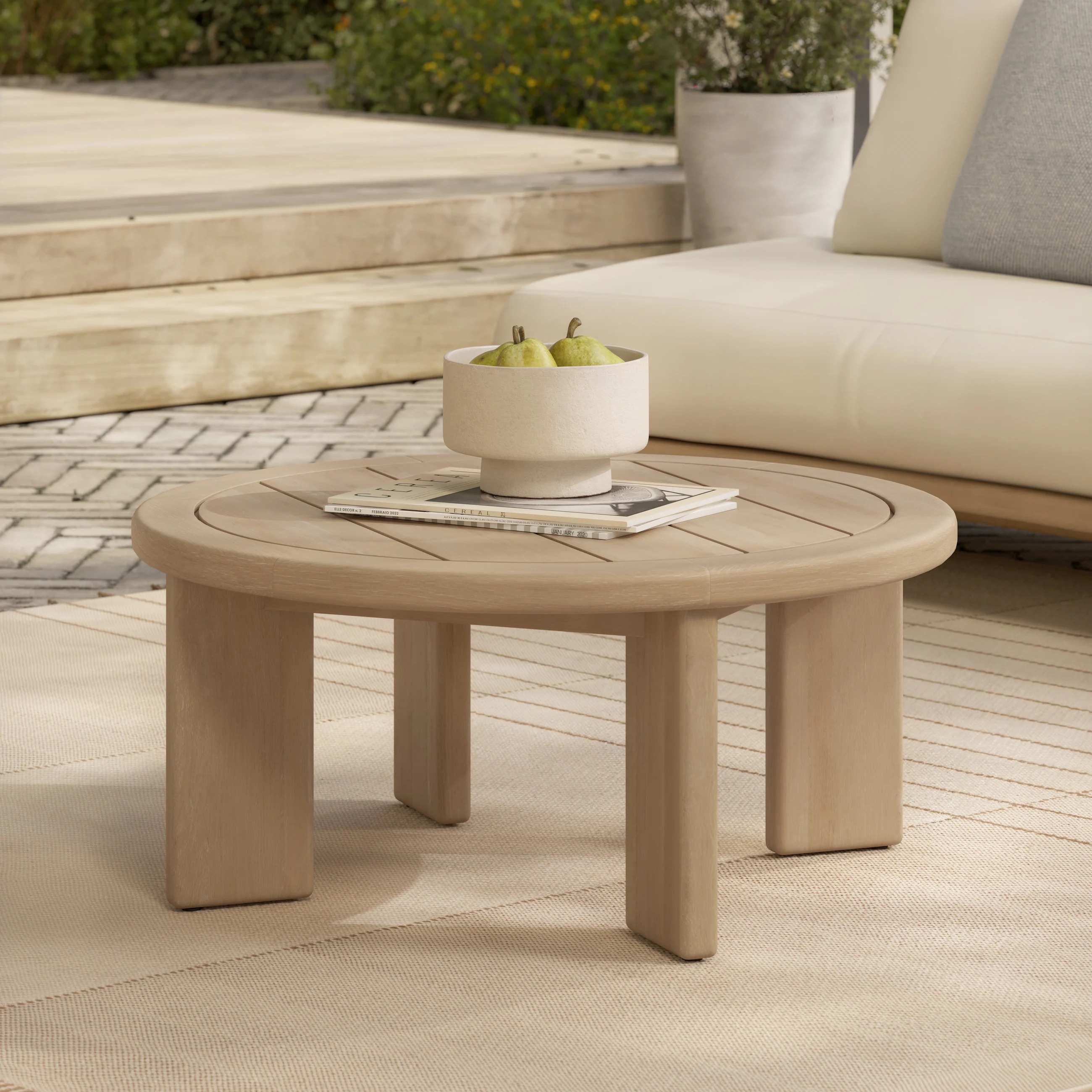 Round wooden coffee table with a fruit bowl and open book, set on a patio near outdoor furniture