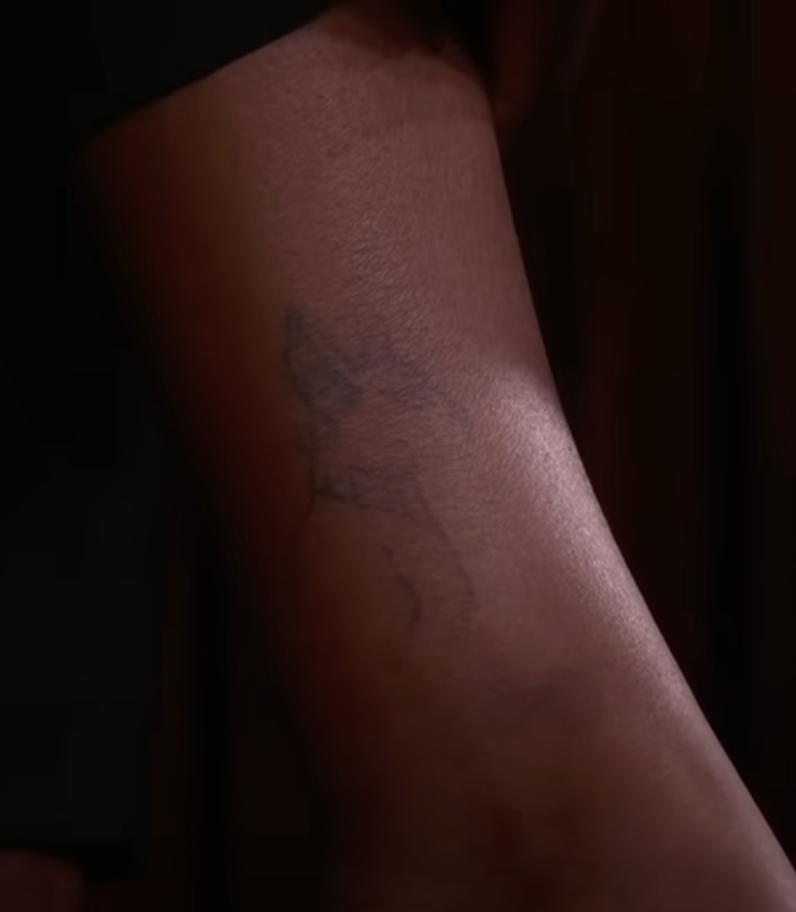 A close-up of Simone's ankle featuring a faint outline of a sphynx cat tattoo